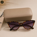Tortoiseshell sunglasses with purple lenses on a beige surface next to a beige case.