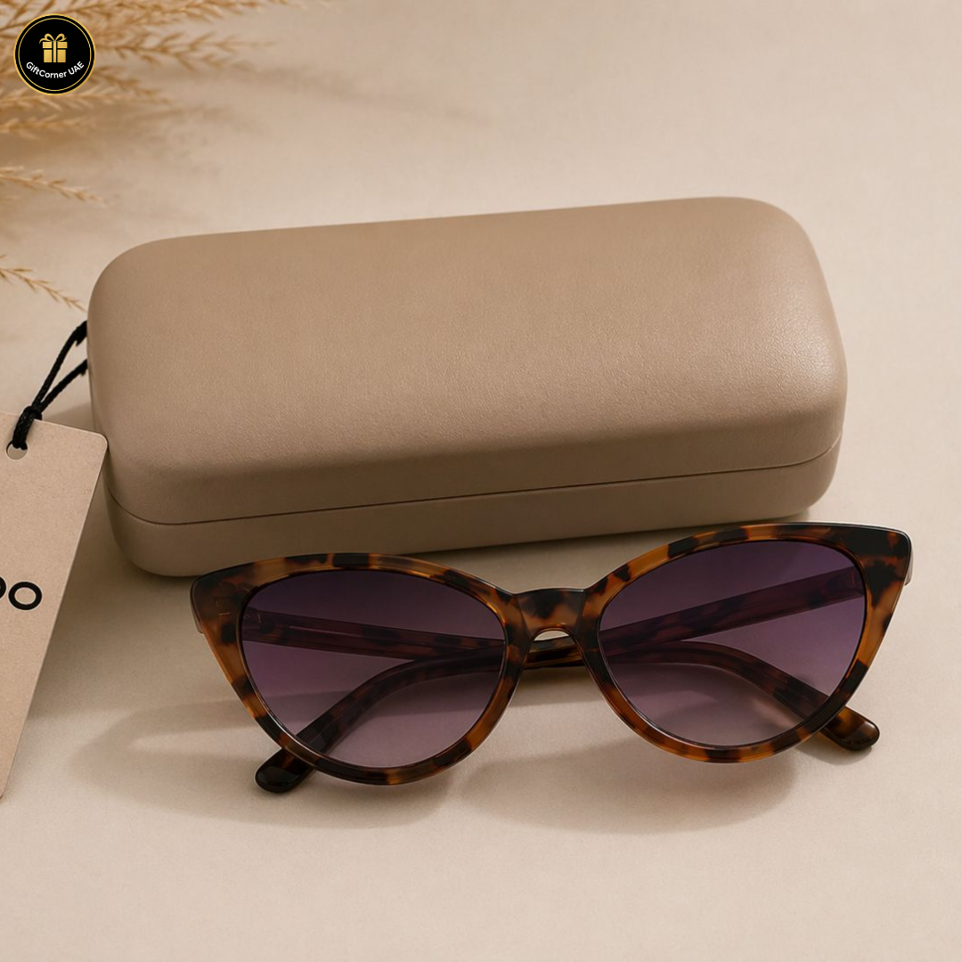 Tortoiseshell sunglasses with purple lenses on a beige surface next to a beige case.