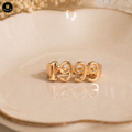 Gold ring with '1999' design on a beige dish
