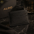 Black leather cardholder with 'ALDO' branding on a dark marble surface.