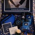 Gift set with Adidas products, including perfume, watch, and chocolate, with a romantic photo in the background.