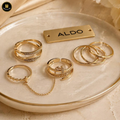 Set of gold rings on a ceramic dish with 'ALDO' branding.